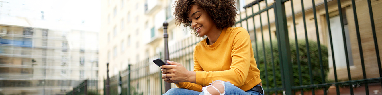 Woman sitting on curb looking at her smartphone