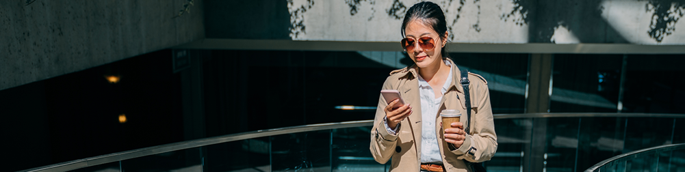 woman walking and looking at phone, while holding to-go coffee
