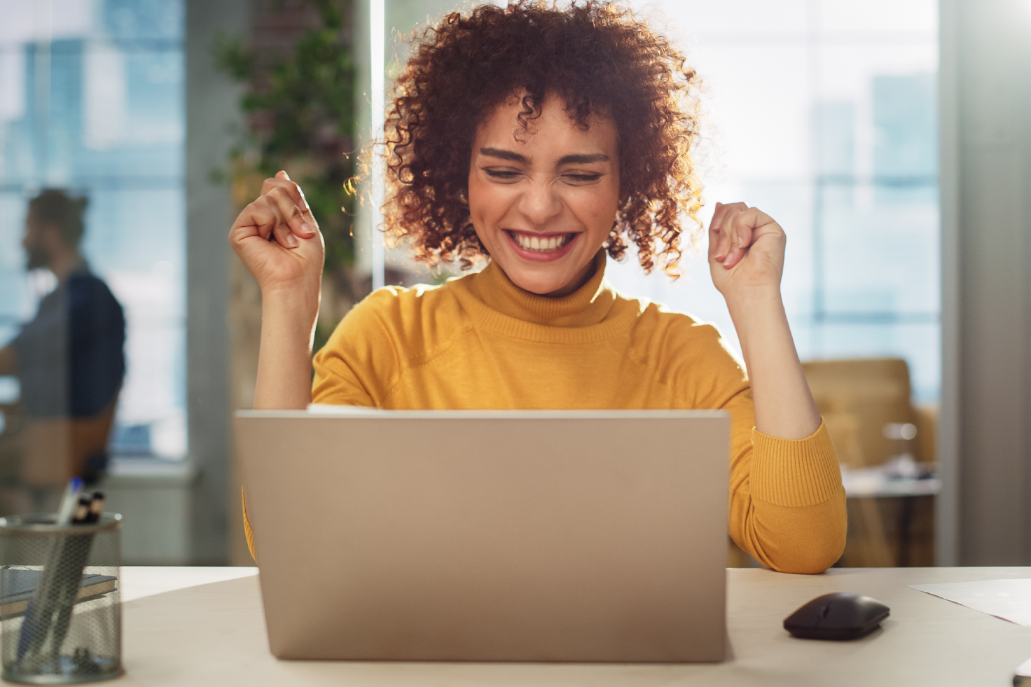 woman in yellow sweater, excitedly looking at laptop