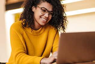 woman in yellow sweater, excitedly looking at laptop